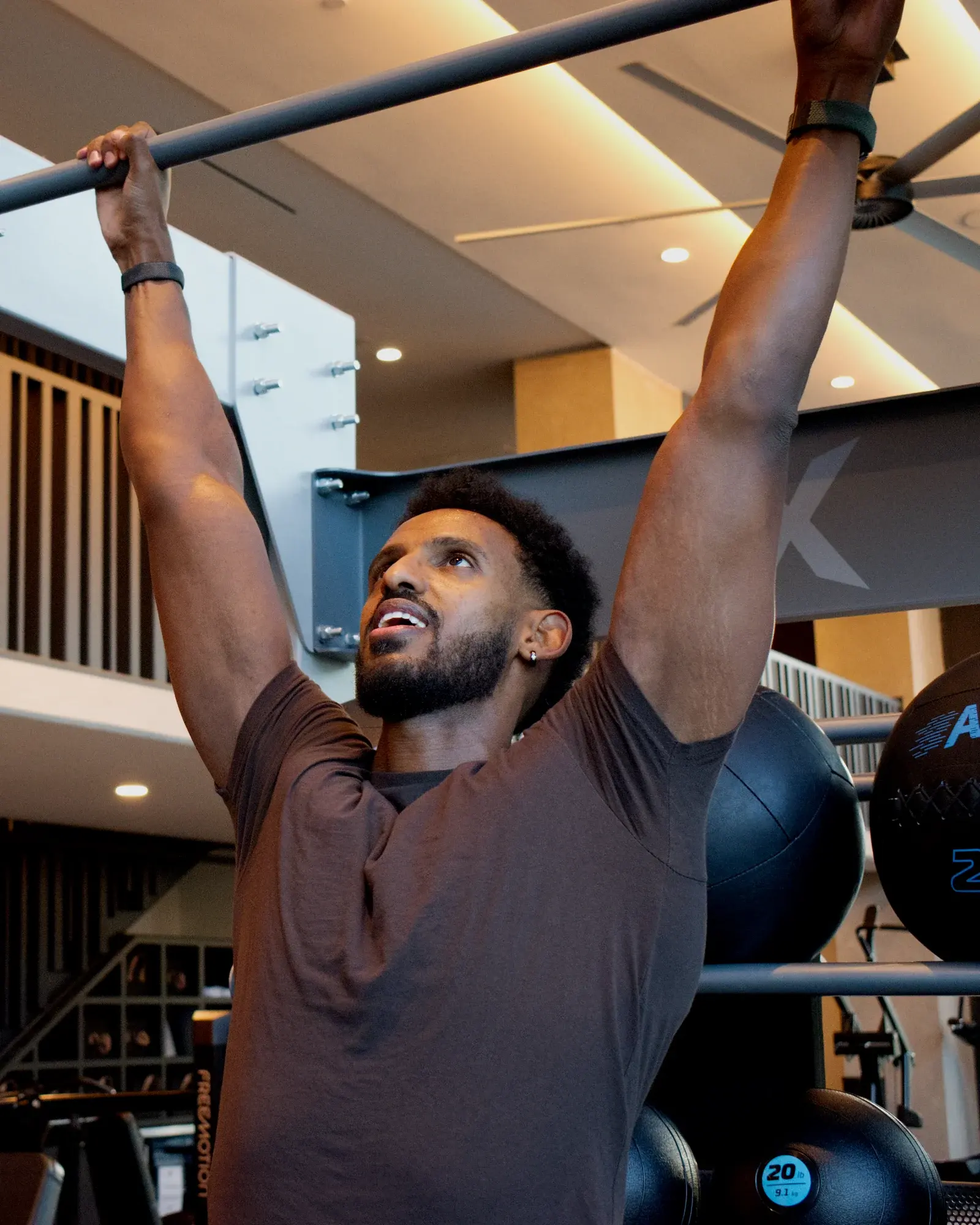 Nathnael Gebre gripping a pull-up bar in a bright, modern gym.